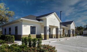 Exterior of Muni Strings’ new location at 2637 W State Road 426 in Oviedo, FL, featuring a modern, light-colored building with dedicated parking and landscaped surroundings.